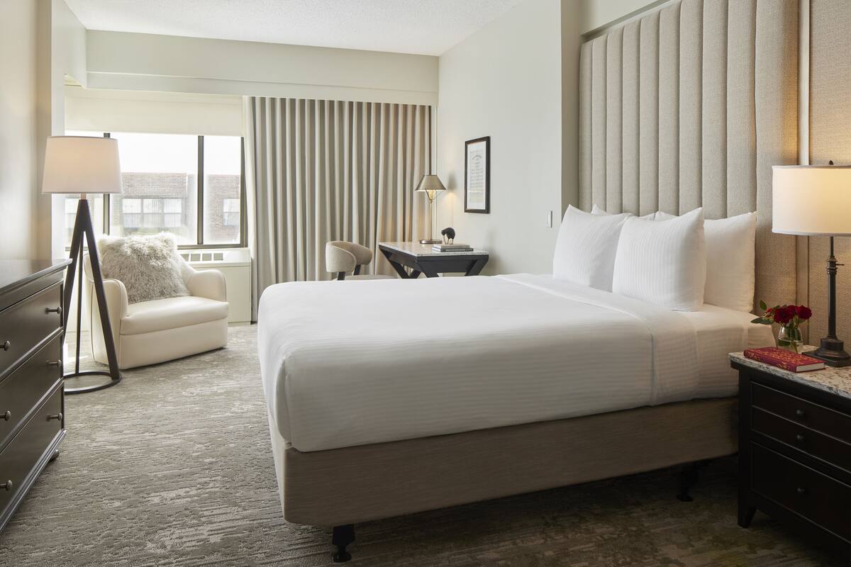 A hotel room with a large bed, a desk, a chair, and a dresser.