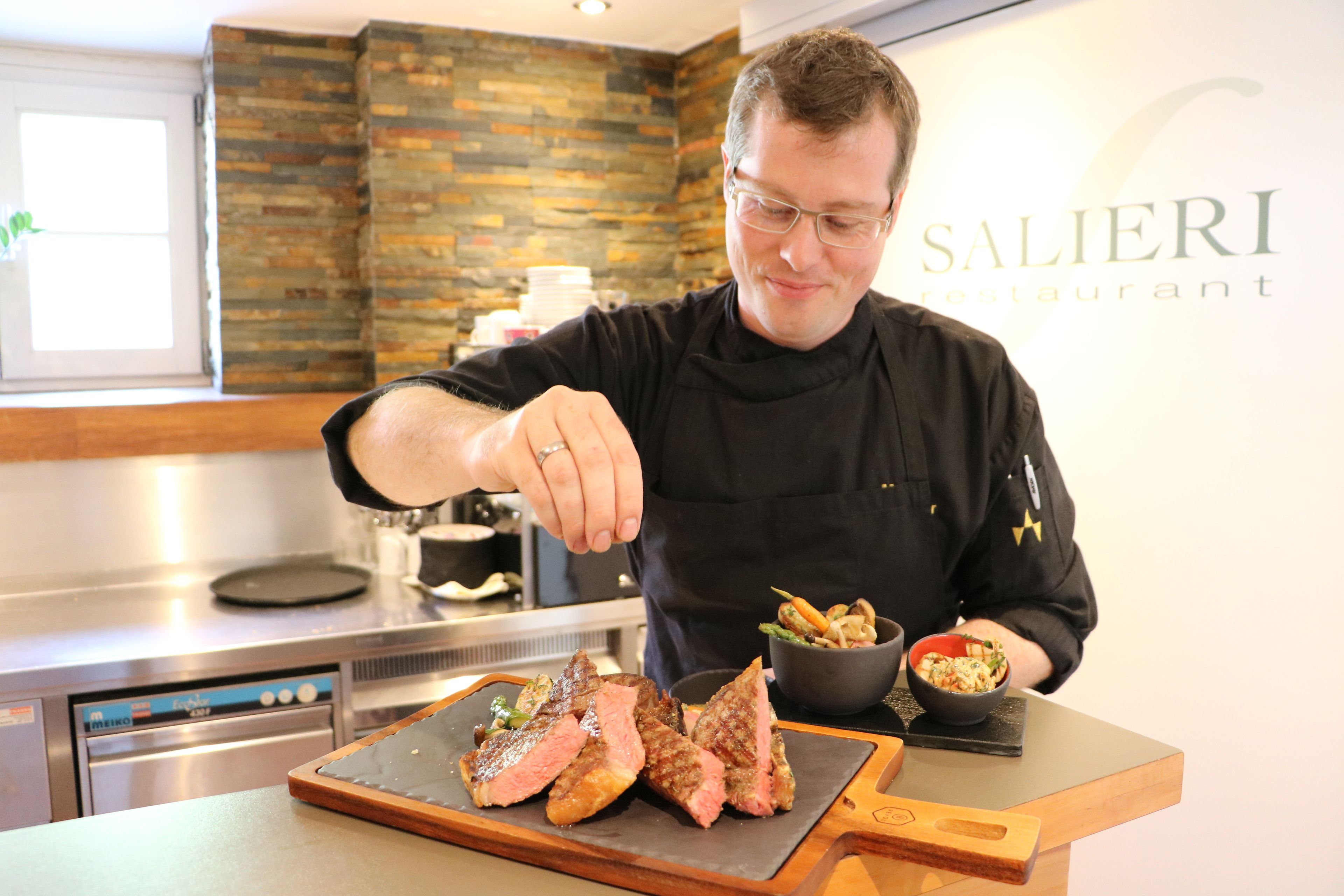 Un chef preparando comida en la cocina de un restaurante con un salpicadero de piedra y electrodomésticos modernos.