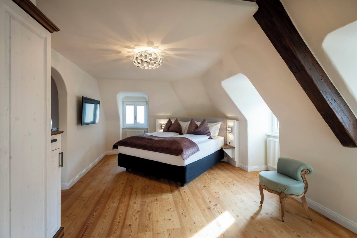 Une chambre avec un grand lit, un plancher en bois, un lustre et une fenêtre.