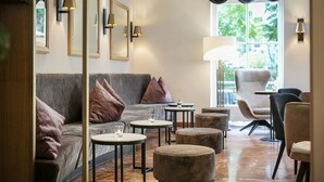 Un espace détente moderne avec un canapé gris, des tables rondes et une grande fenêtre agrémentée de rideaux.