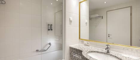 Un baño moderno con ducha envuelta en vidrio, lavamanos de granito y un espejo grande con marco dorado.