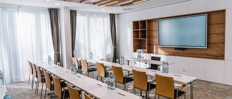 A conference room with a long table, chairs, a flat-screen TV, and a wooden shelf.