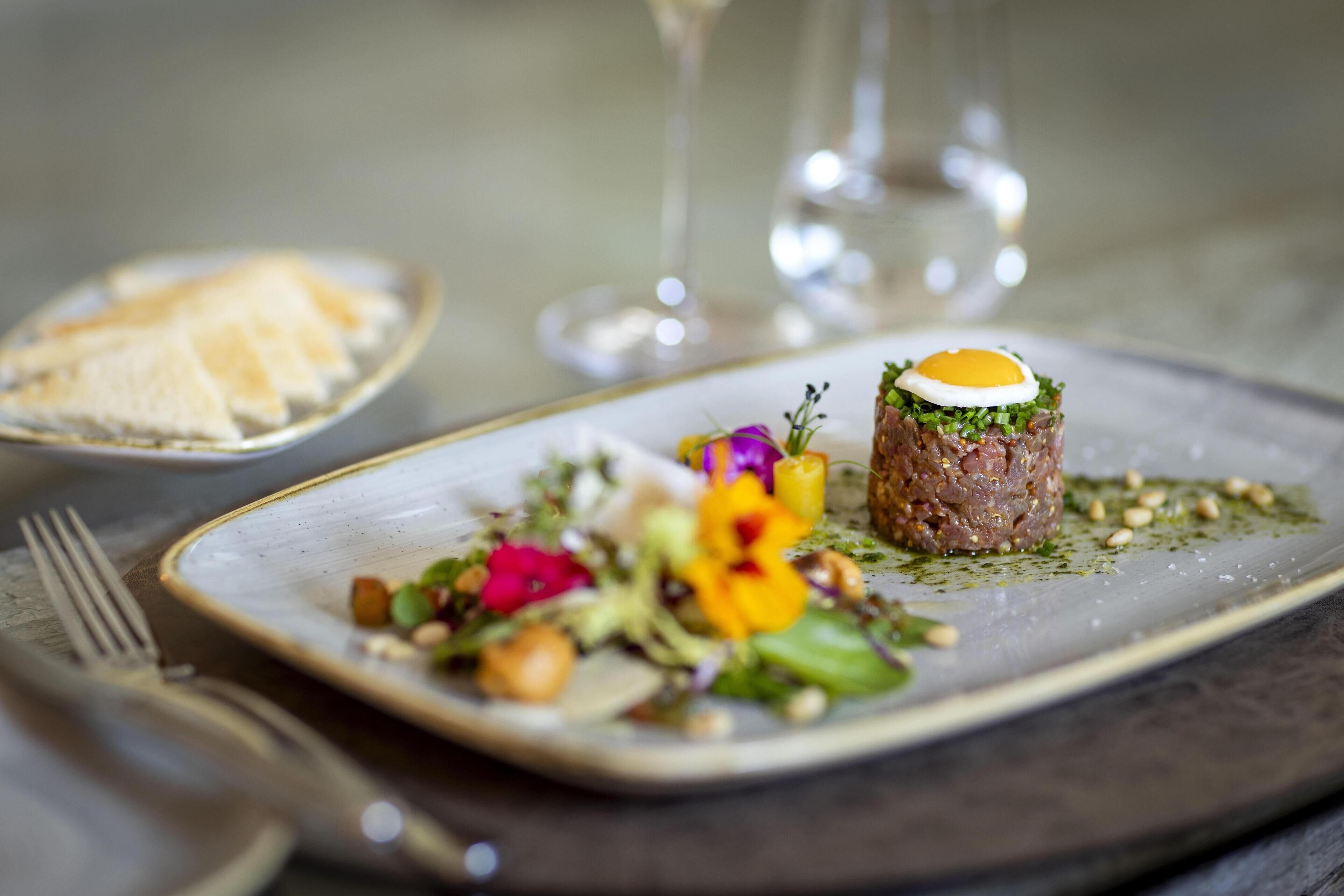 Un plat composé d’une galette de viande centrale, d’un œuf et de légumes verts, accompagné d’une salade et de pain.