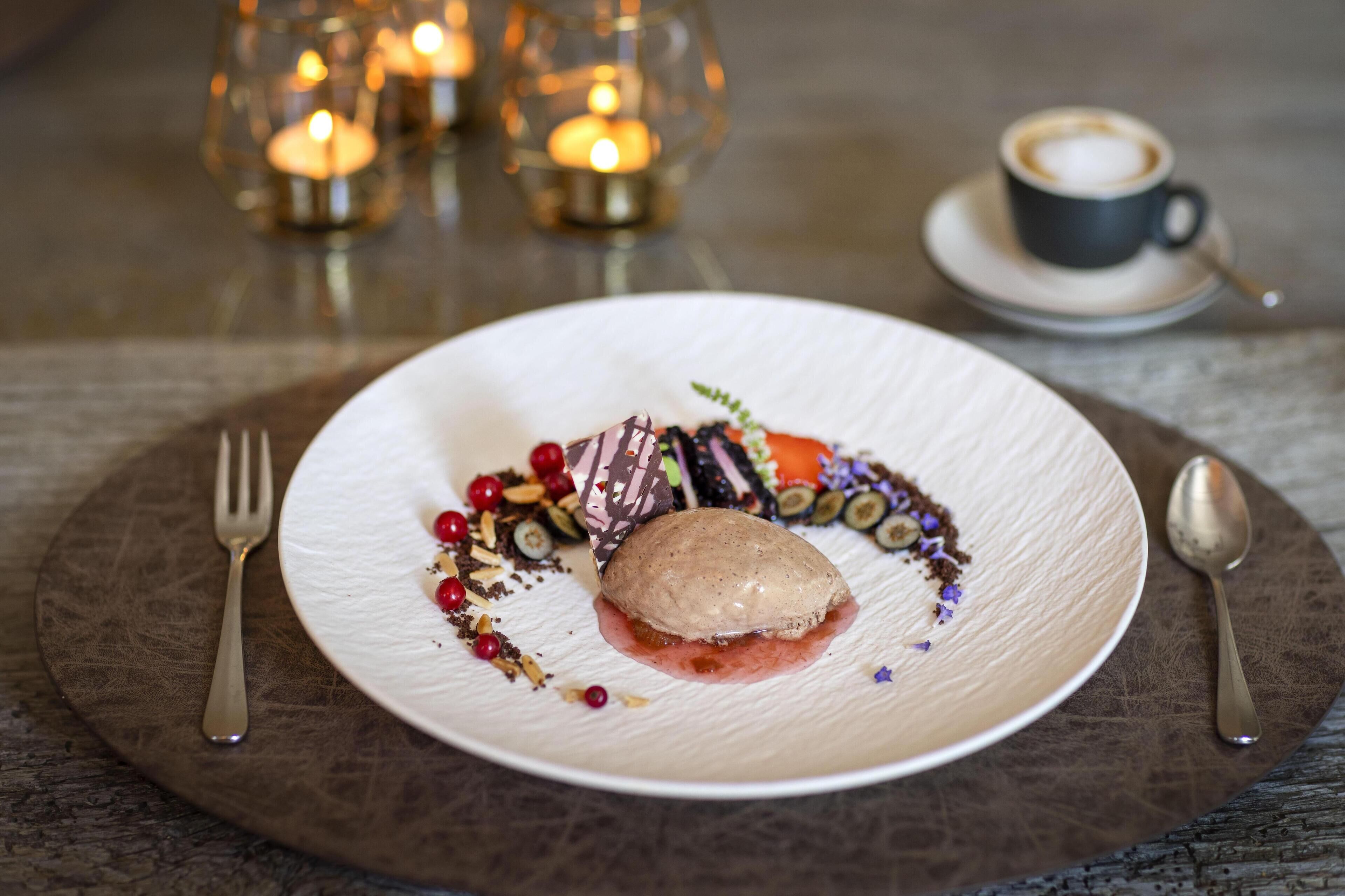 Ein Dessert auf einem weißen Teller mit Gabel und Löffel auf einem runden, braunen Tisch.