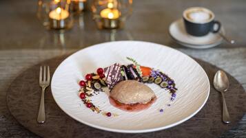 Ein Dessert auf einem weißen Teller mit Gabel und Löffel auf einem runden, braunen Tisch.
