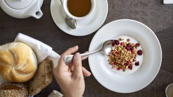 A breakfast setting with a cup of coffee, a plate of yogurt with granola and berries, a teapot, and a croissant.