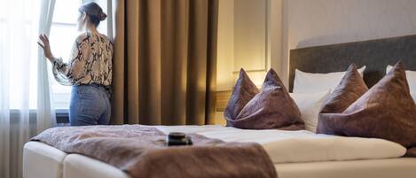 A hotel room with a large bed, a headboard with multiple pillows, and a window with curtains.