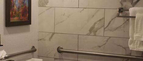 A bathroom with a toilet, marble tiles, a handrail, a towel rack, and a framed painting on the wall.