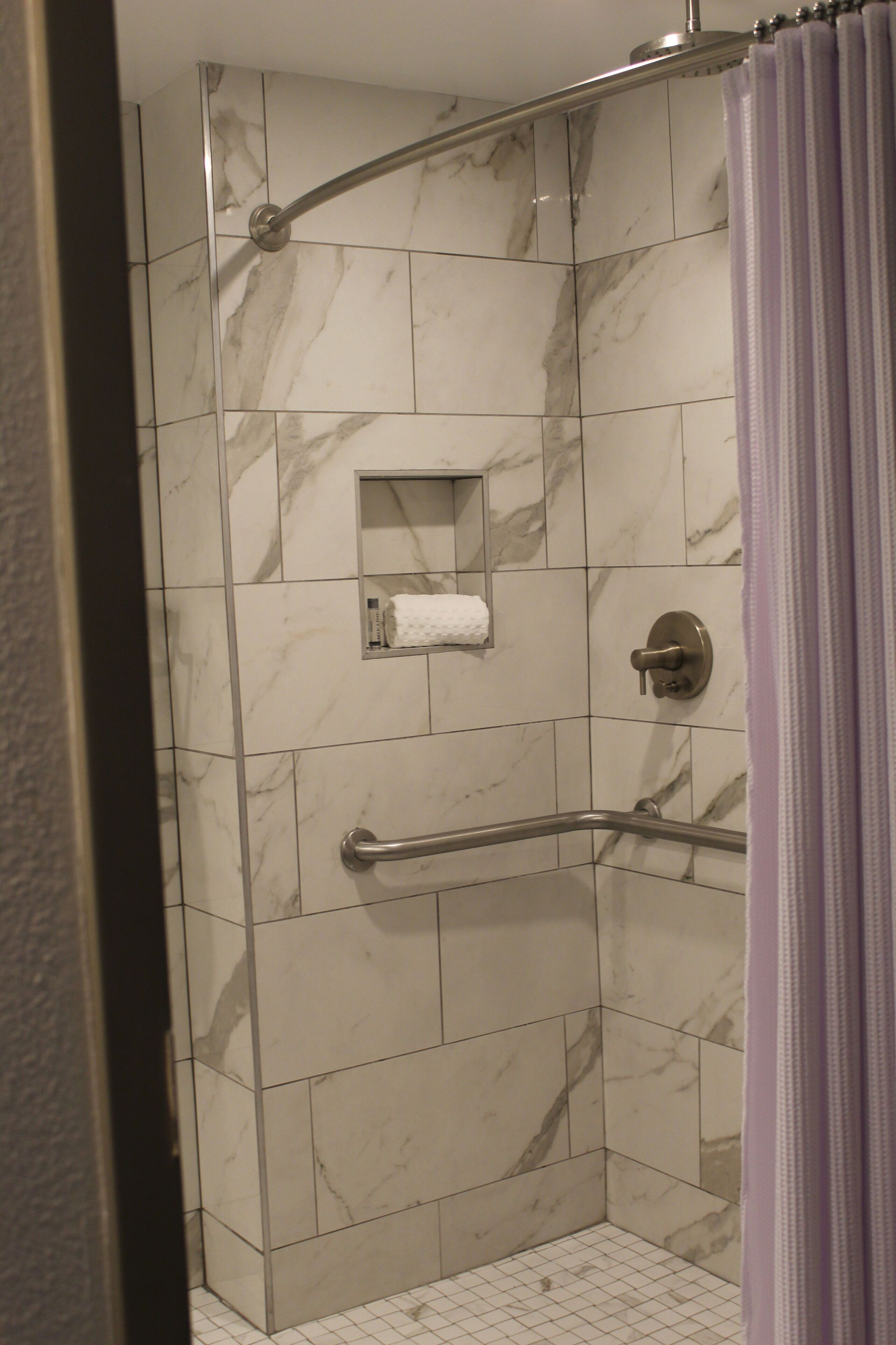 A shower with a grab bar, marble tiles, and a towel rack.