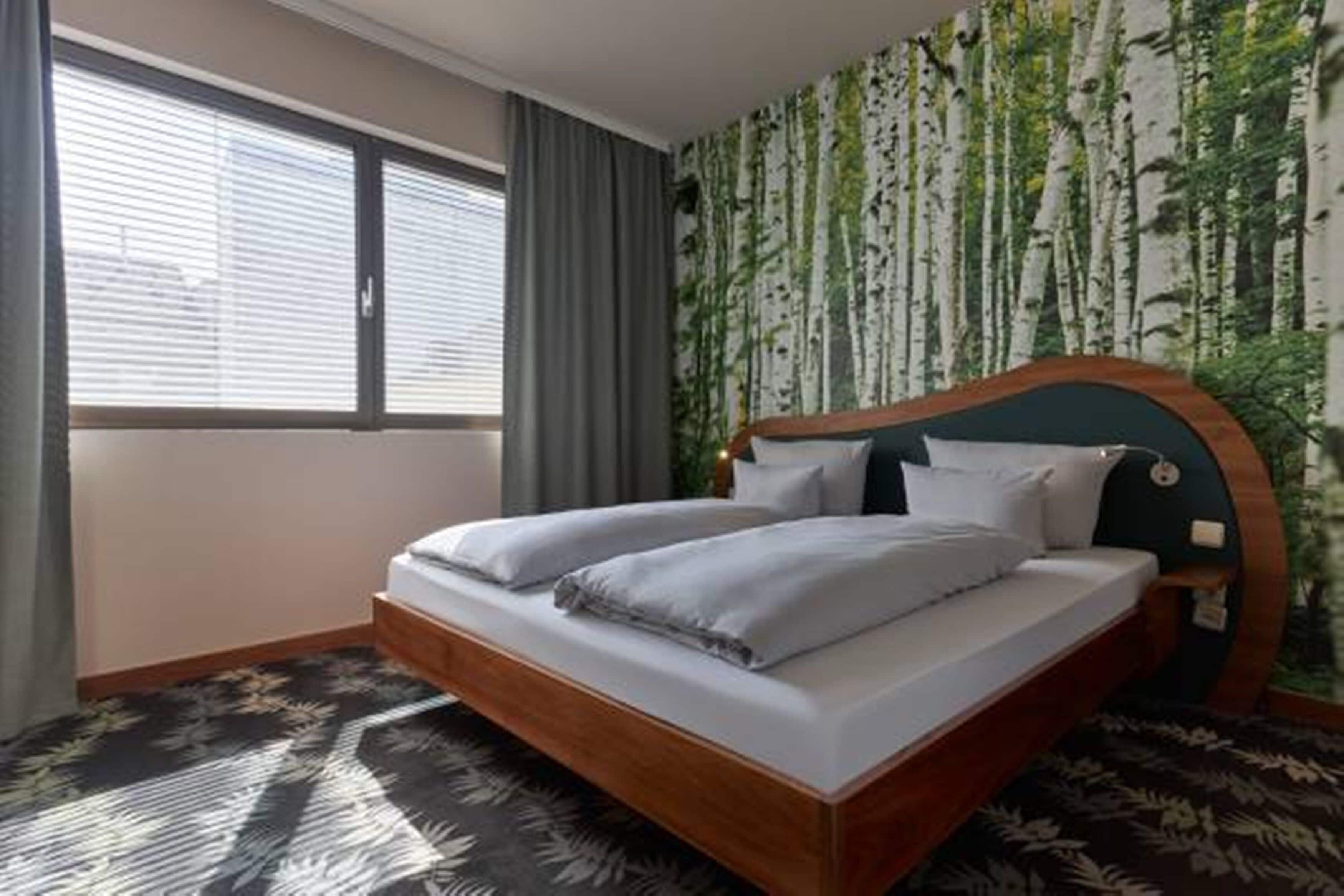 A bedroom with a bed, a window, and a wall with a tree pattern.