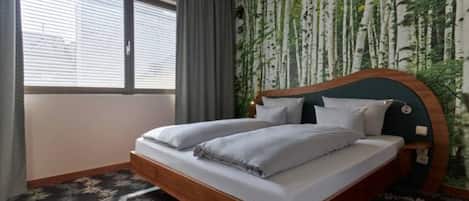 A bedroom with a bed, a window, and a wall with a tree pattern.