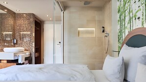 Una habitación de hotel moderna con una cama grande, un baño con cabina de ducha de vidrio y un lavamanos sobre la pared.