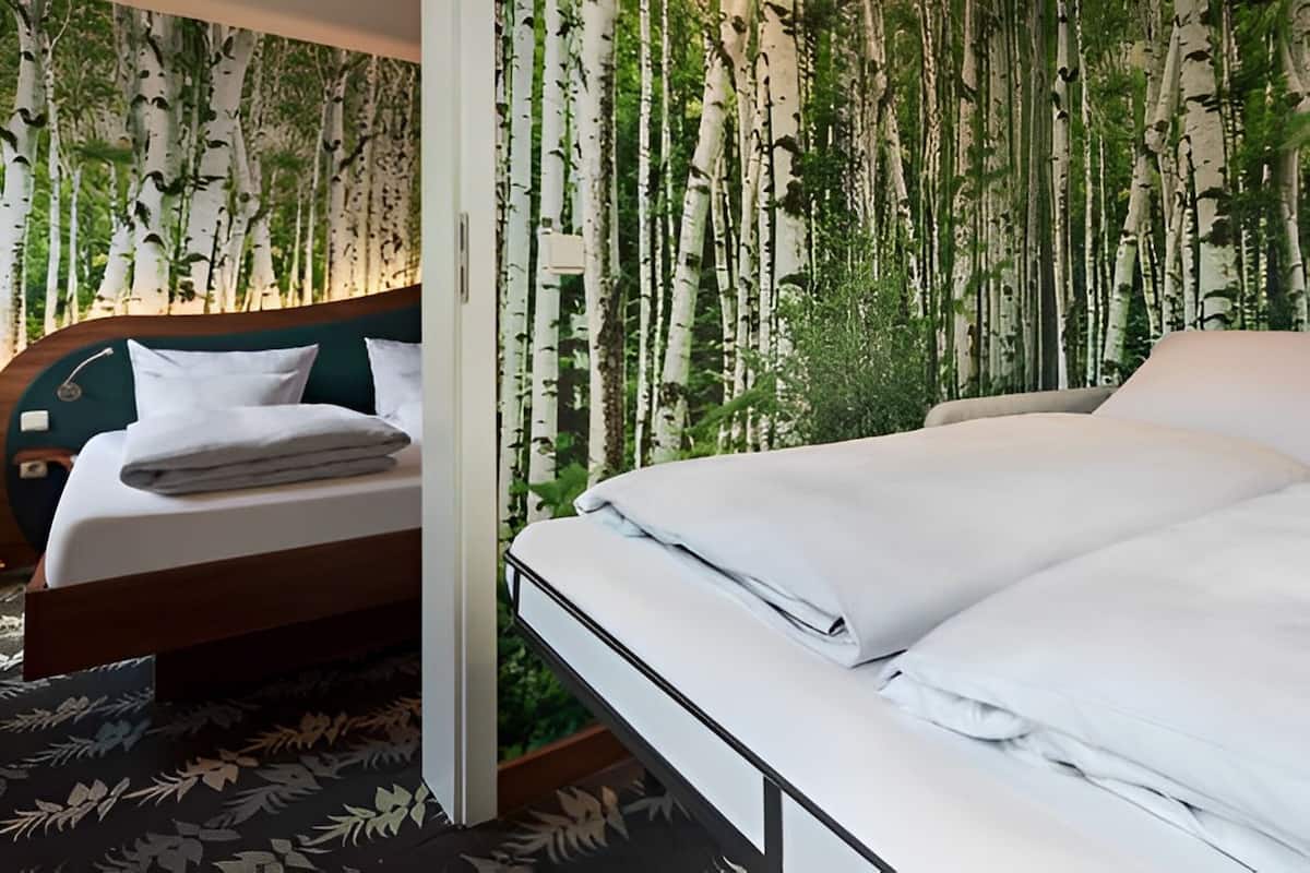A hotel room with two beds, a wooden headboard, and a wall with a nature-themed wallpaper.