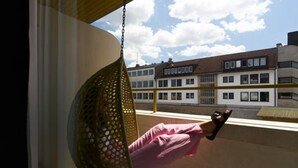 Una persona sentada en una hamaca colgante junto a una ventana que da a un edificio con varias ventanas y balcones.