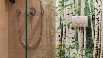 A bathroom with a glass shower enclosure, a toilet, and a wall with a forest wallpaper.