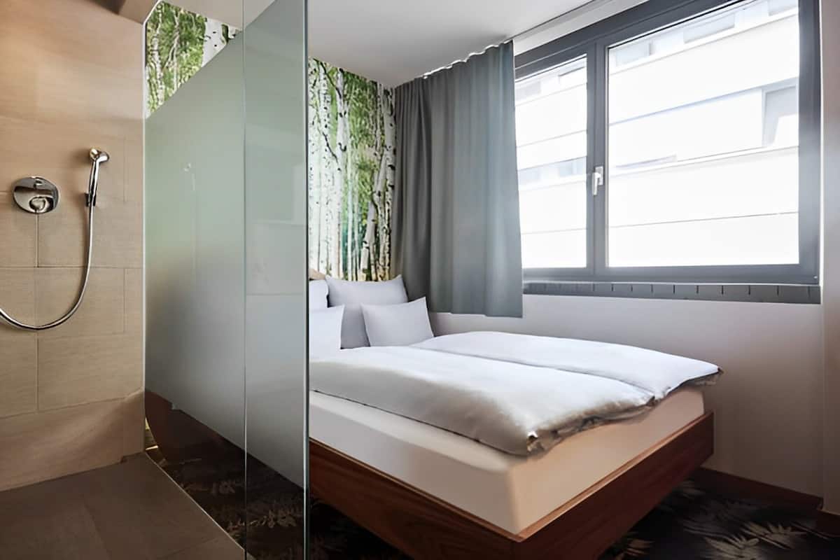 A hotel room with a bed, a shower, and a window with curtains.