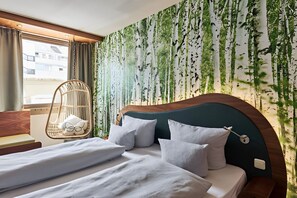A hotel room with a bed, a hanging chair, and a wall with a nature-themed wallpaper. - Cocoon München Stachus (Munich)