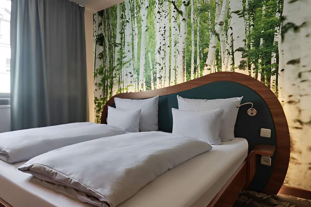 A double bed with white linens in a hotel room with a green headboard and a window with curtains.