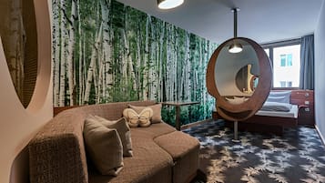 Ein modernes Hotelzimmer mit einem großen Fenster, einem runden Spiegel, einer Couch mit dekorativen Kissen und einem gemusterten Teppich.