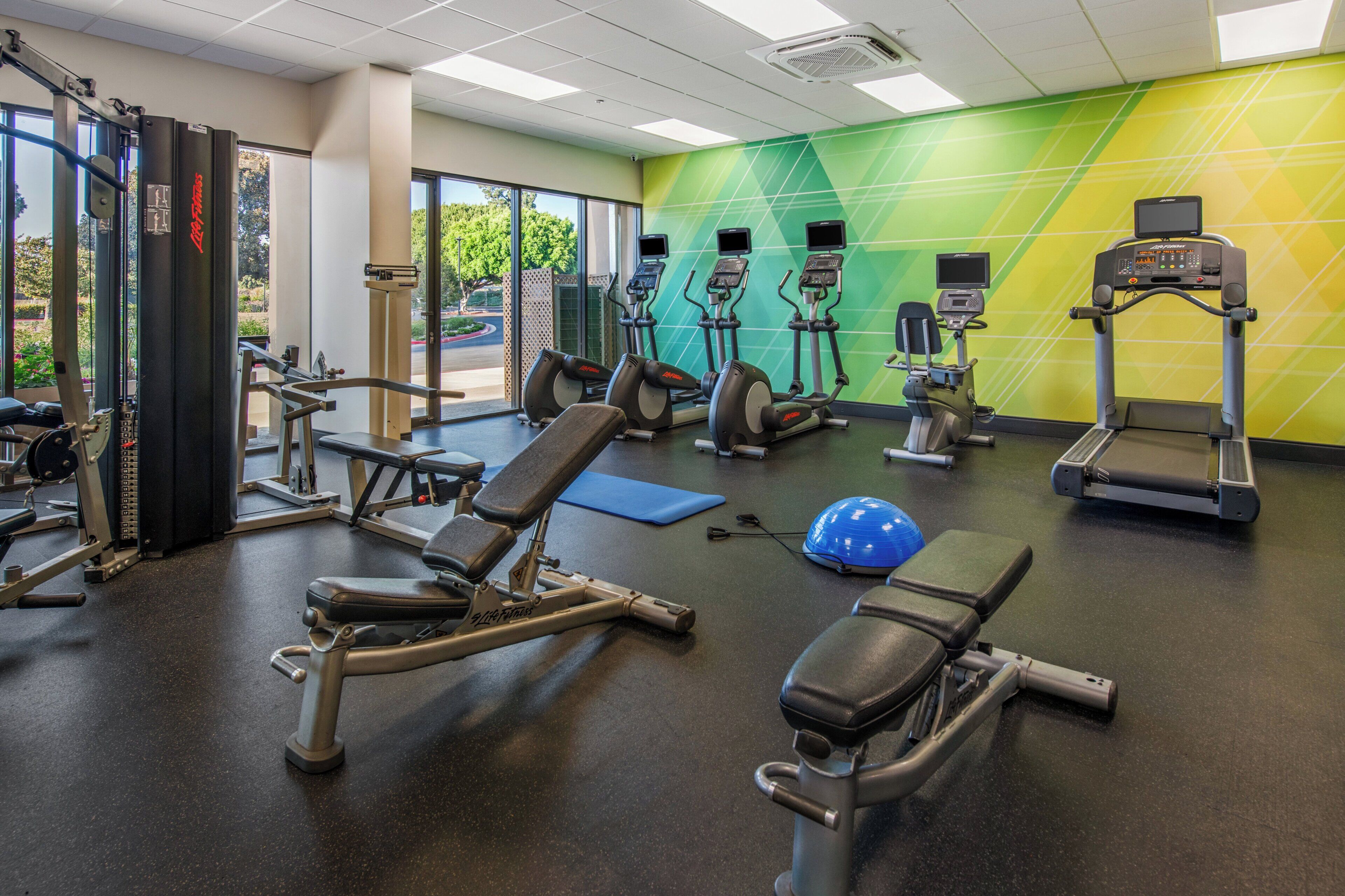 Un gimnasio con equipamiento de ejercicio, una colchoneta azul y una pared con un diseño geométrico.
