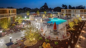 A well-lit outdoor pool area with lounge chairs and umbrellas, surrounded by landscaped gardens and modern buildings. - Holiday Inn Oxnard – Ventura by IHG (Oxnard)