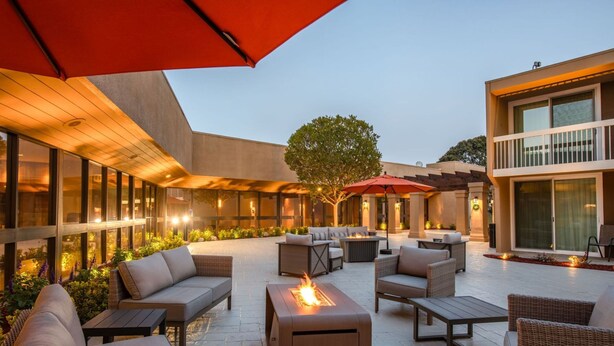 An outdoor patio area with wicker furniture, a fire feature, and a large red umbrella. - Holiday Inn Oxnard – Ventura by IHG (Oxnard)