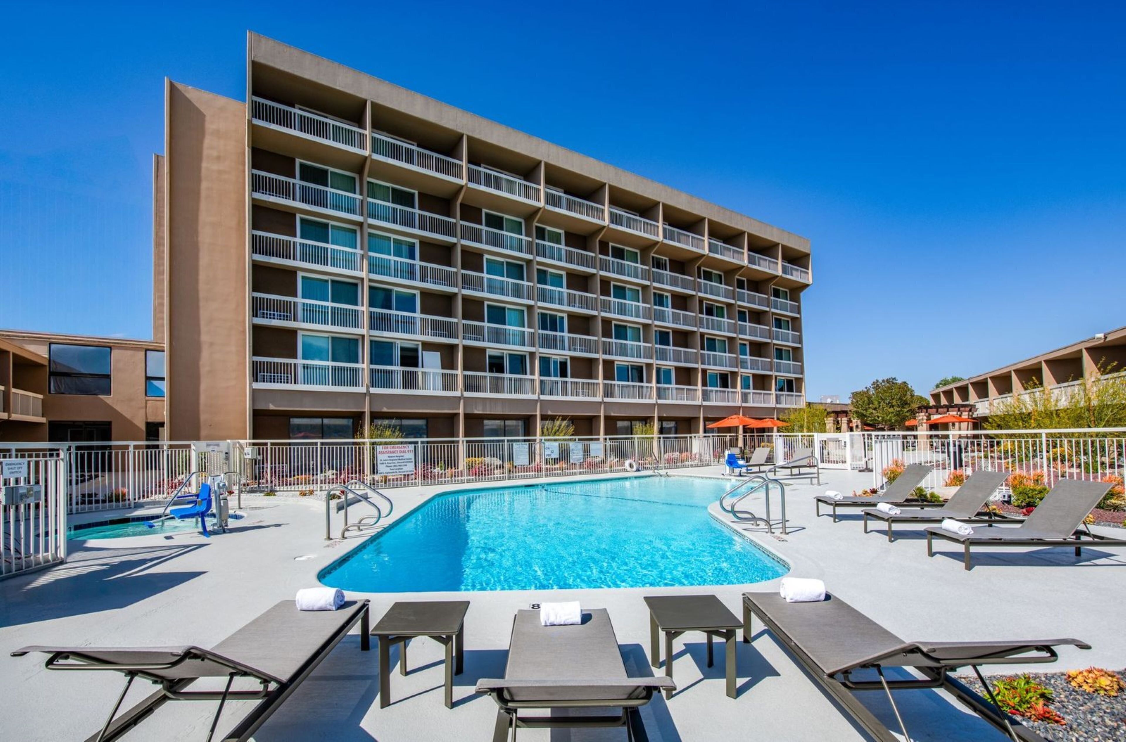A hotel with a swimming pool, lounge chairs, and a multi-story building with balconies.