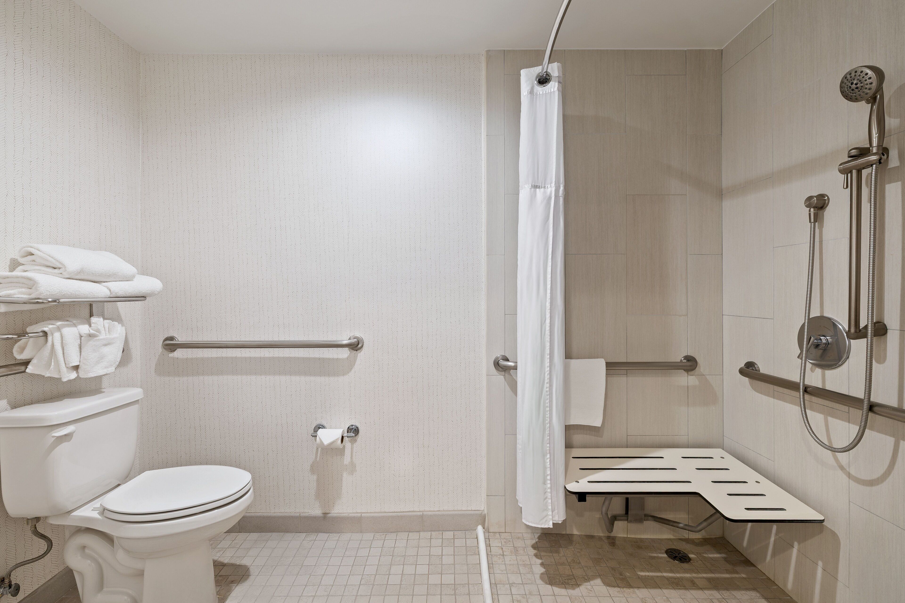 Un baño con inodoro, ducha con barra de apoyo y toallero.