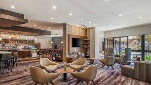 A modern hotel lobby with a bar area, seating arrangements, and a large window offering a view of the outdoors. - Holiday Inn Oxnard – Ventura by IHG (Oxnard)