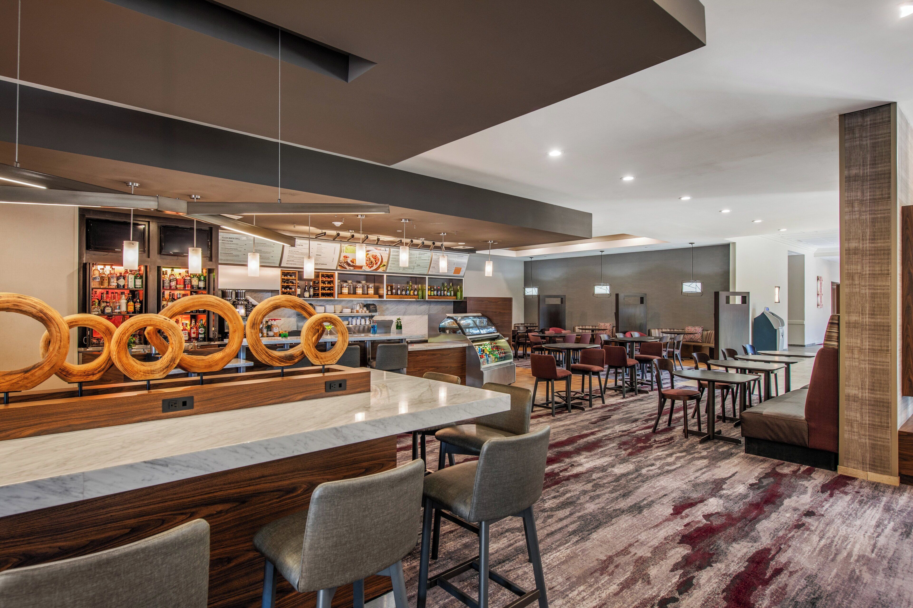 Un hall d’hôtel moderne doté d’un bar, de différents espaces aménagés pour s’asseoir et d’un sol recouvert de moquette.