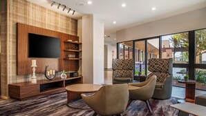 A modern lobby with a large TV, comfortable seating, a wooden entertainment unit, and a view of the outdoors. - Holiday Inn Oxnard – Ventura by IHG (Oxnard)