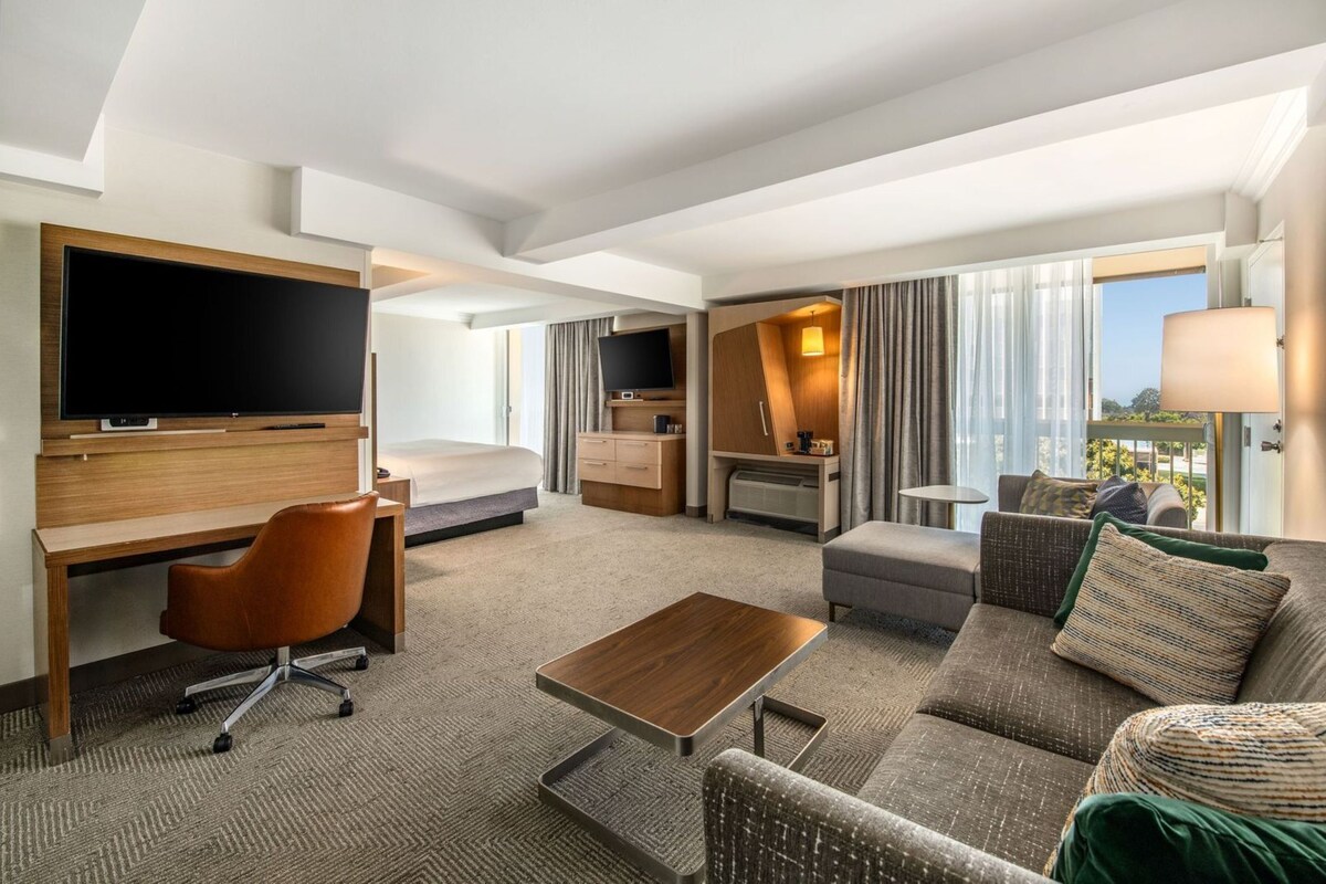 A modern hotel room with a flat-screen TV, a desk, a comfortable sofa, and a bed.
