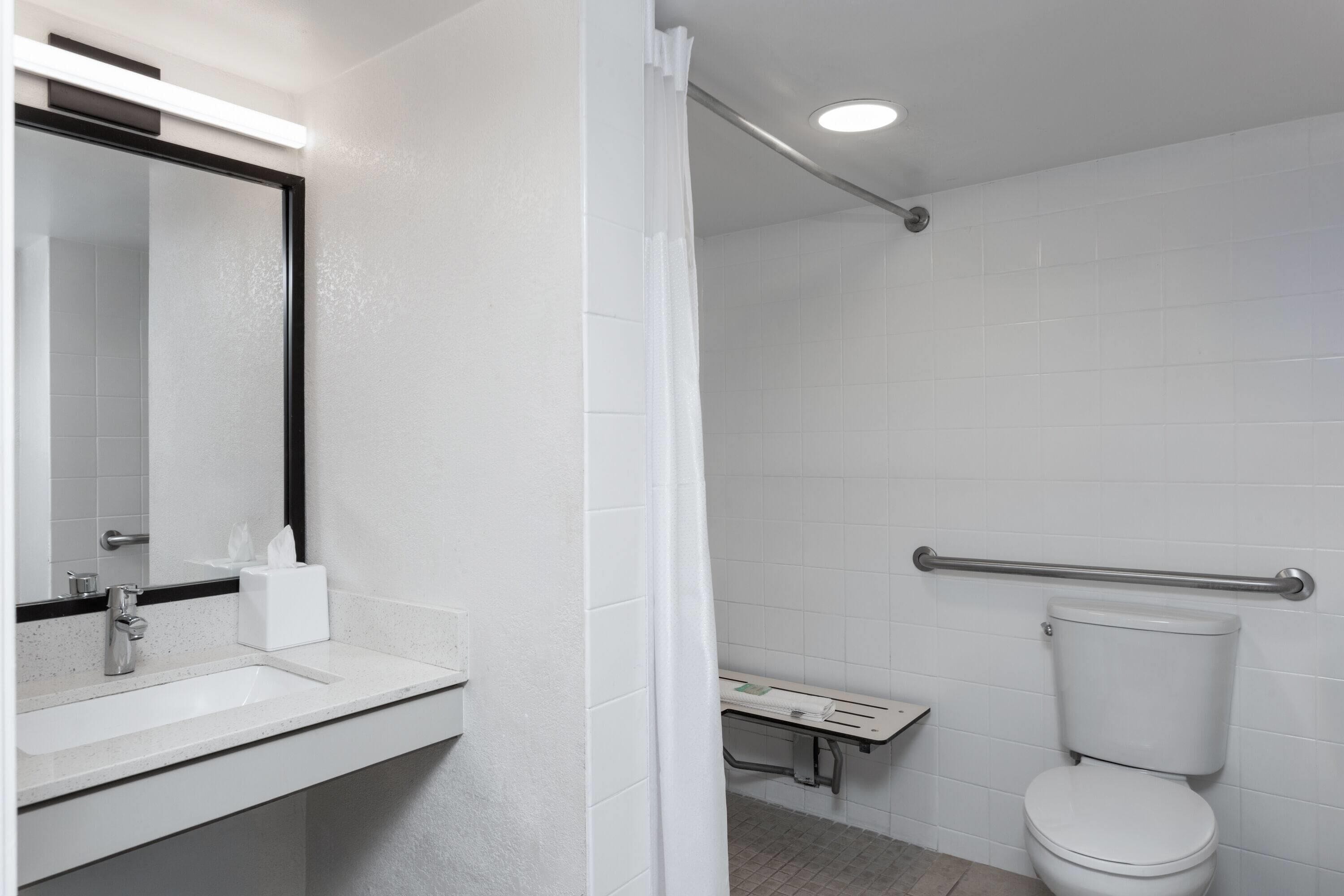 Een badkamer met een wit wastafelmeubel, spiegel en toilet, douchegordijn en een handgreep.