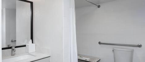 Un baño con lavamanos blanco, espejo, inodoro, cortina de ducha y barra de apoyo.
