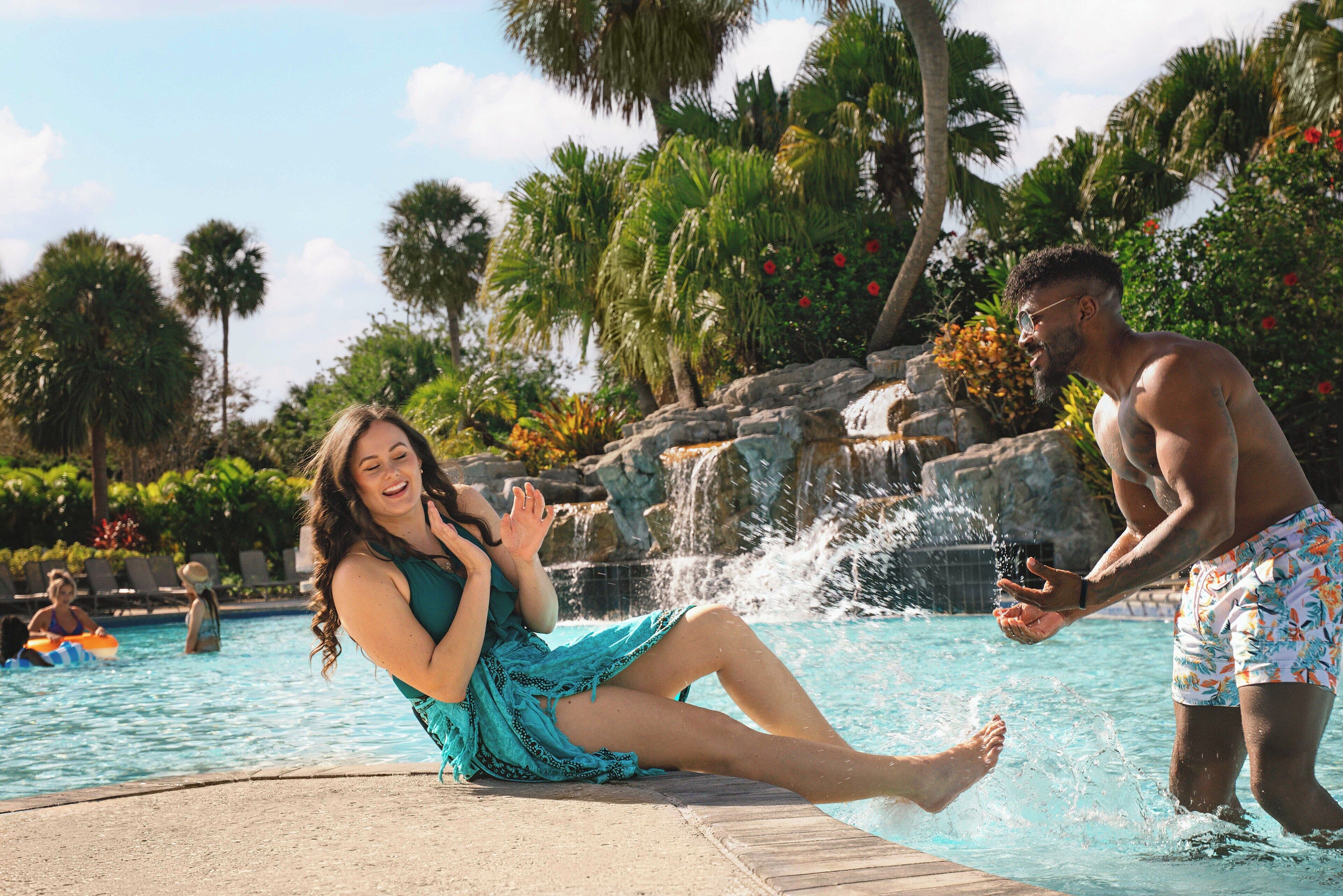 A pool area with a water feature, lounge chairs, and palm trees.