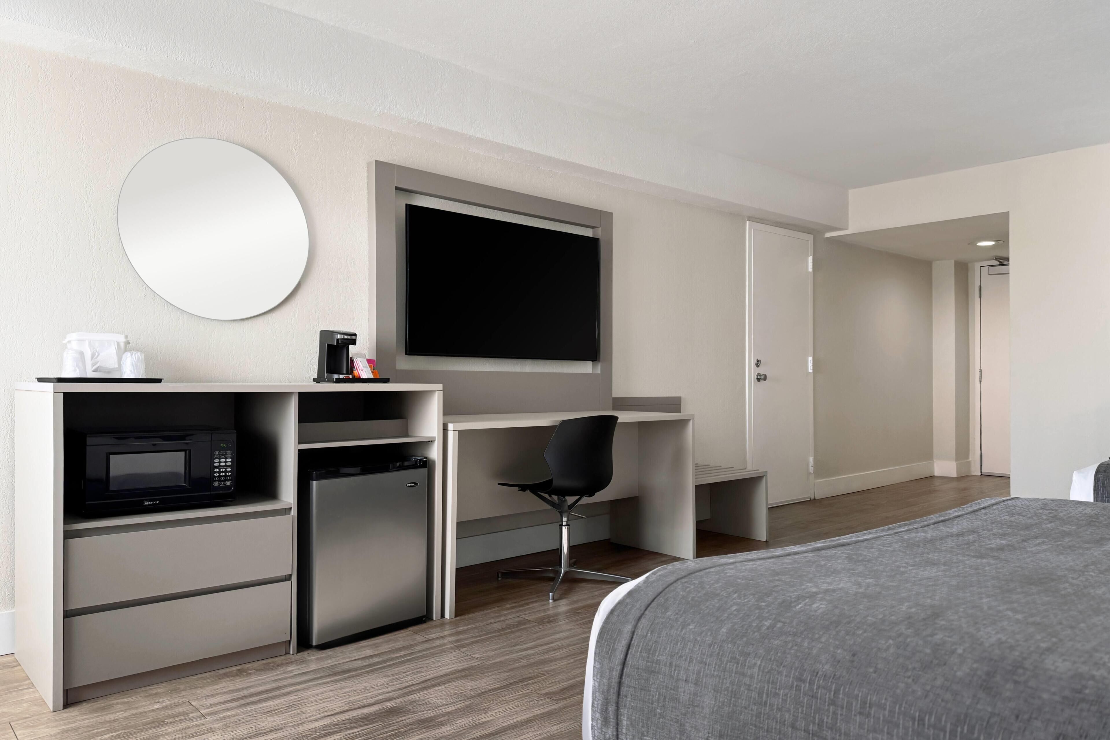 Quarto de hotel moderno com cama, escrivaninha, televisão de tela plana, micro-ondas, frigorífico, cadeira e um espelho grande.
