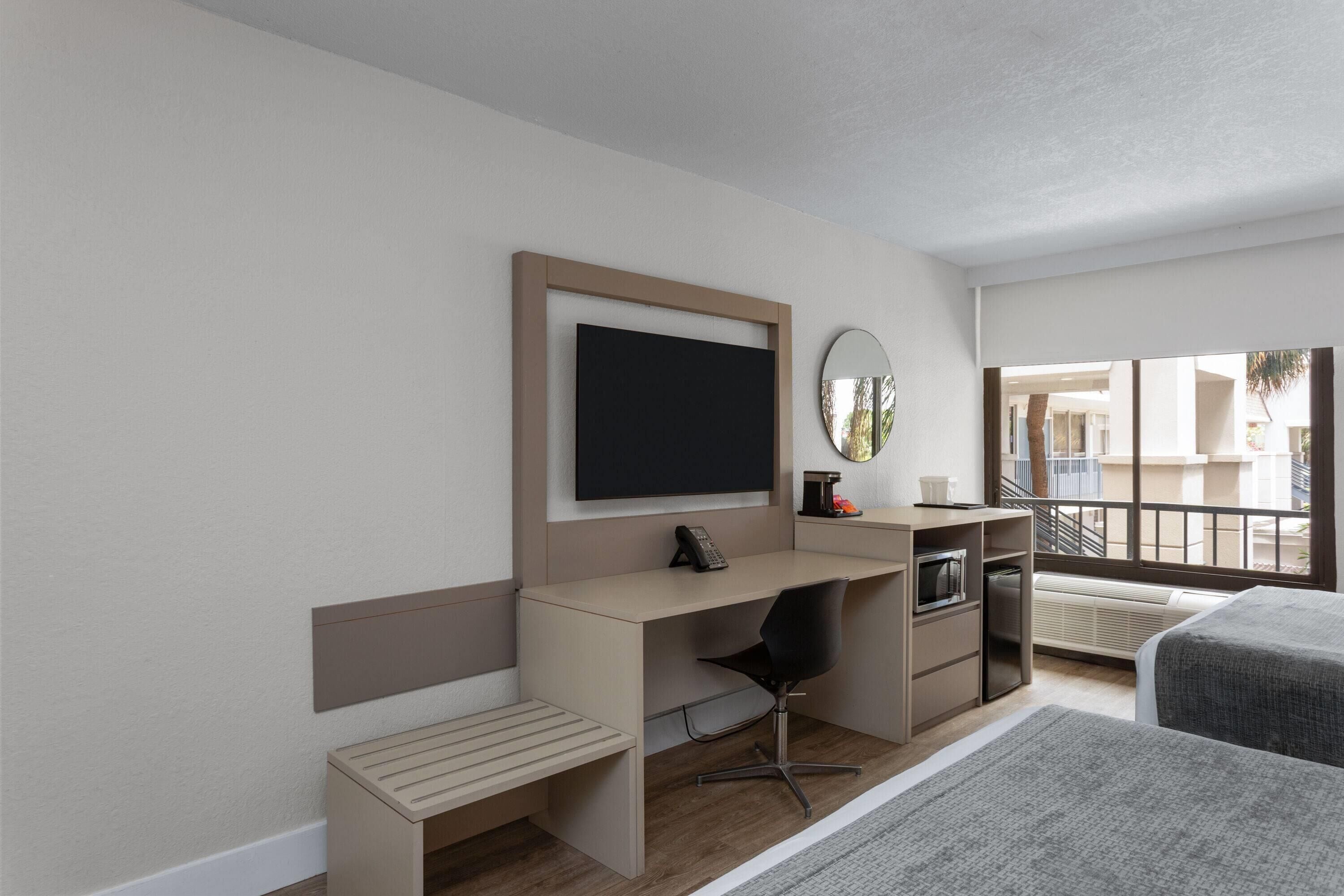 A hotel room with a desk, chair, bed, and a large window with a view.
