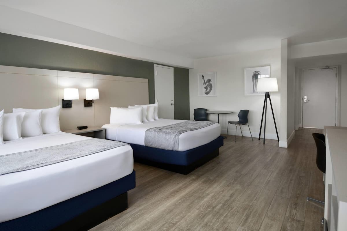 Una camera d'albergo con due letti, una scrivania, una sedia, una lampada e opere d'arte alle pareti.