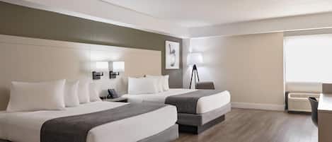 A hotel room with two beds, a desk, a chair, a lamp, and a window.