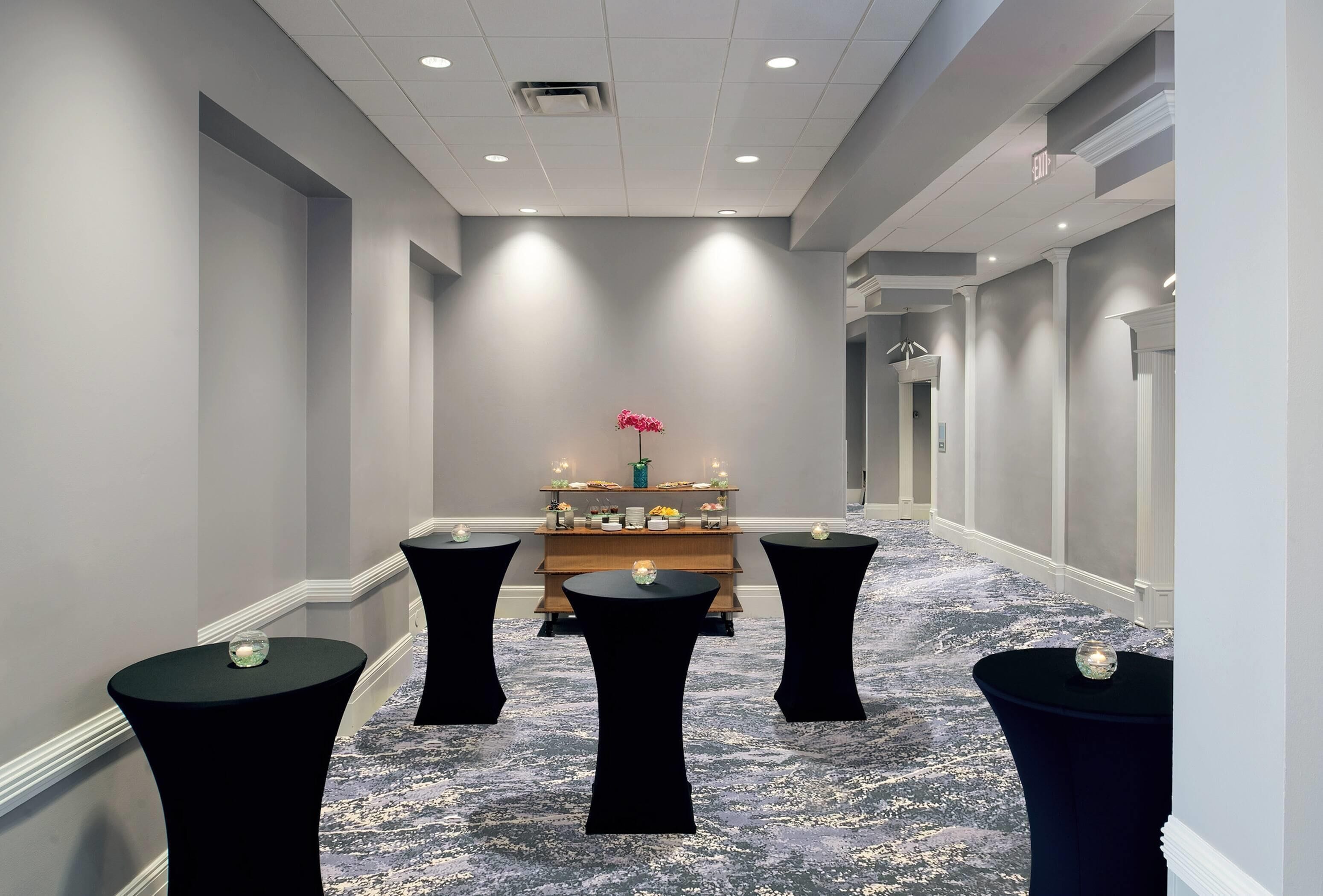 A corridor with a reception desk, black tables with glass candle holders, and a carpeted floor.