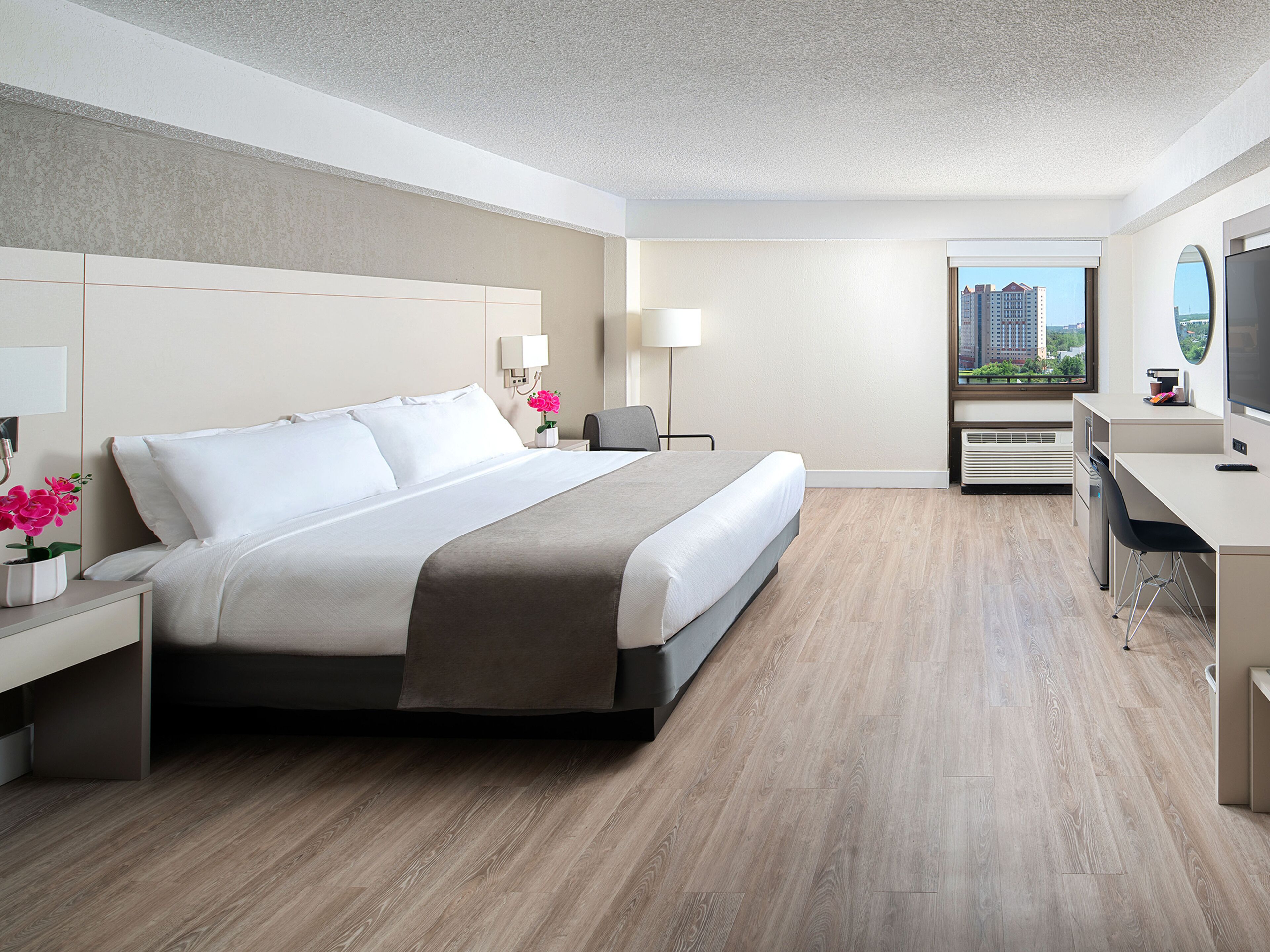 A modern hotel room with a large bed, bedside tables, a desk, and a view of the city.