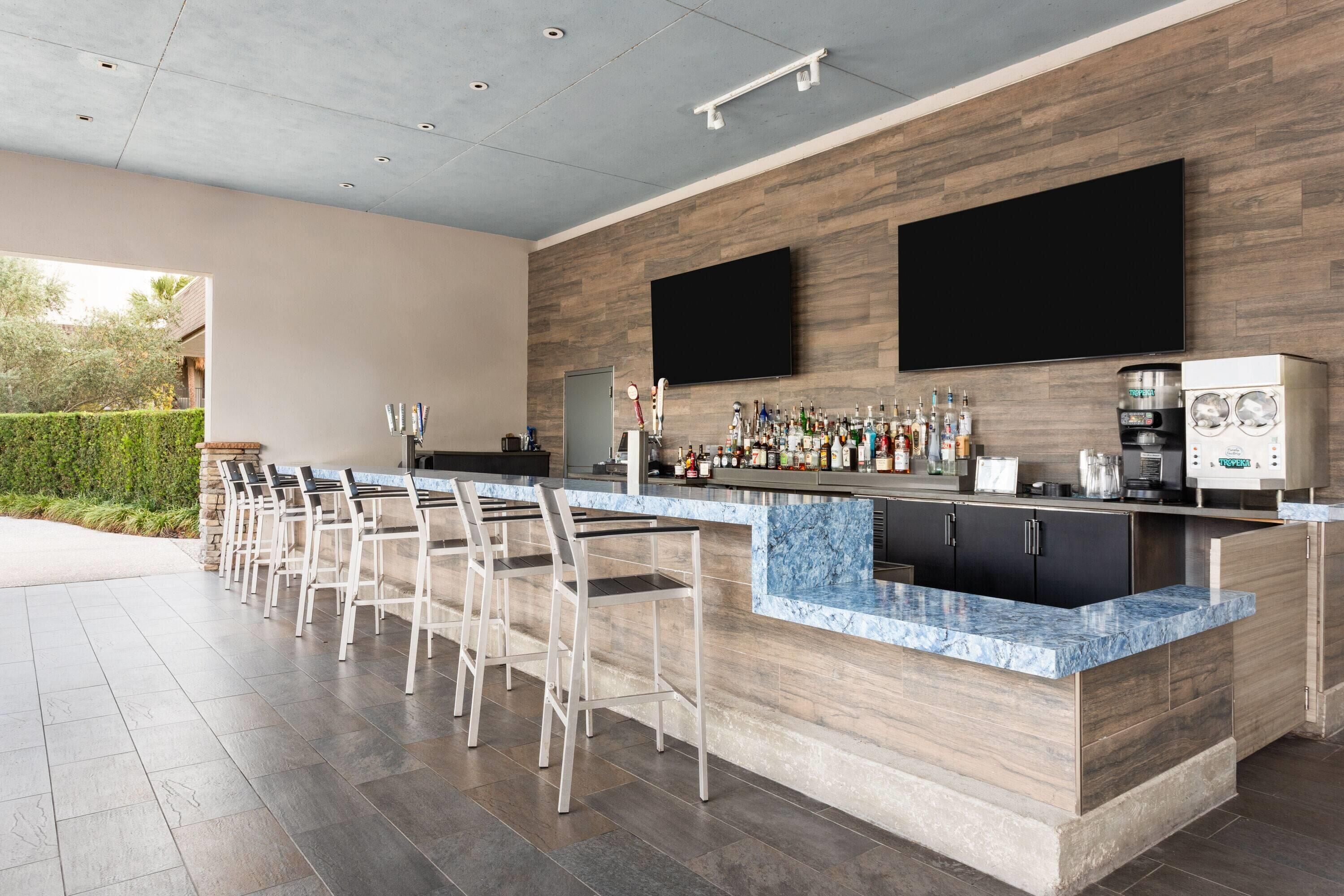 A modern bar area with a marble countertop, bar stools, a flat-screen TV, and a coffee machine.