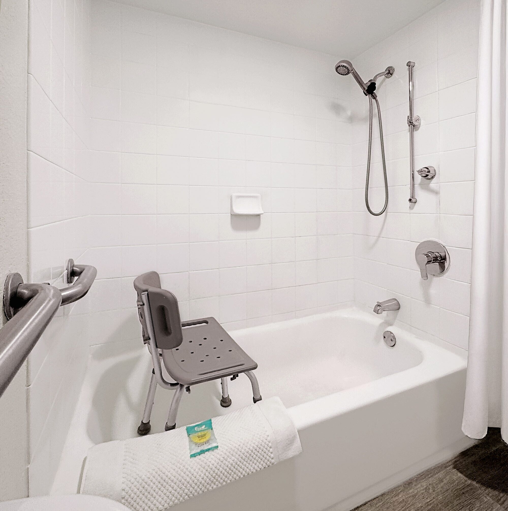 A bathroom with a white bathtub, a shower with a handheld showerhead, and a grab bar for support.
