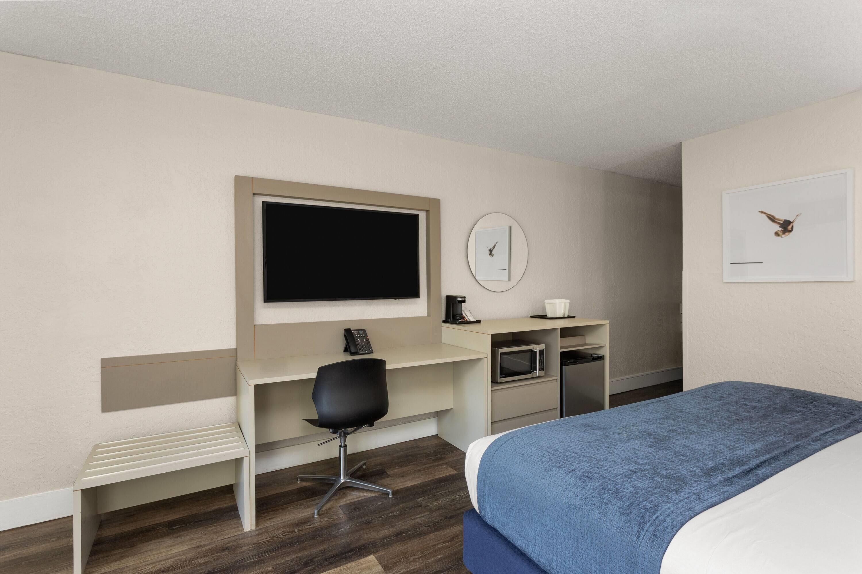 Una camera d'albergo con un letto, una scrivania con una sedia, una televisione, un forno a microonde e una sveglia appesa al muro.