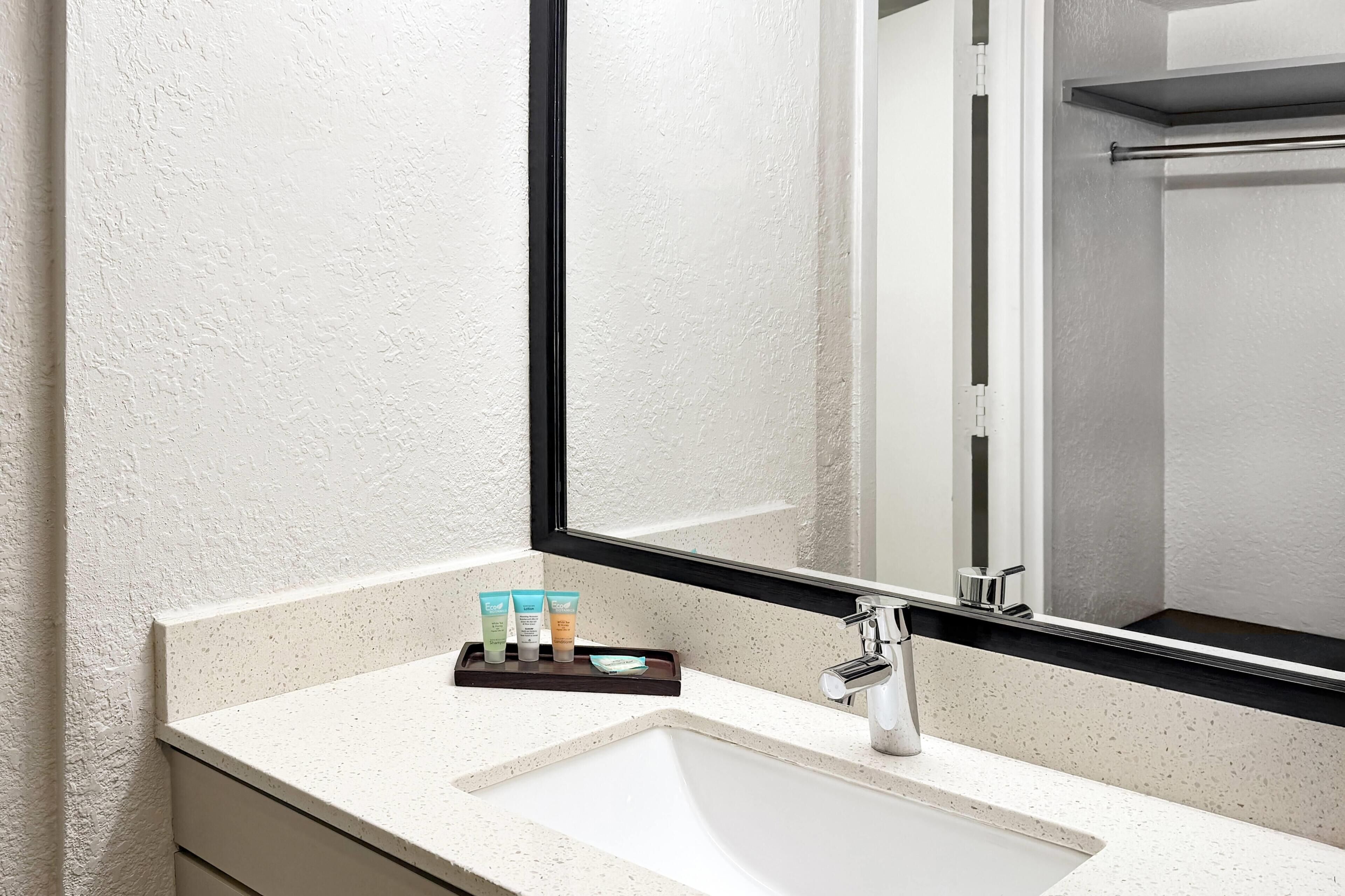 A bathroom with a white sink, a mirror, and a shelf with toiletries.