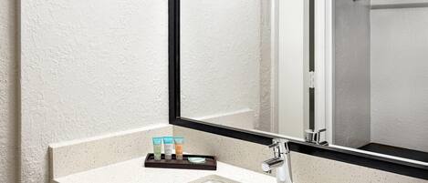 A bathroom with a white sink, a mirror, and a shelf with toiletries.