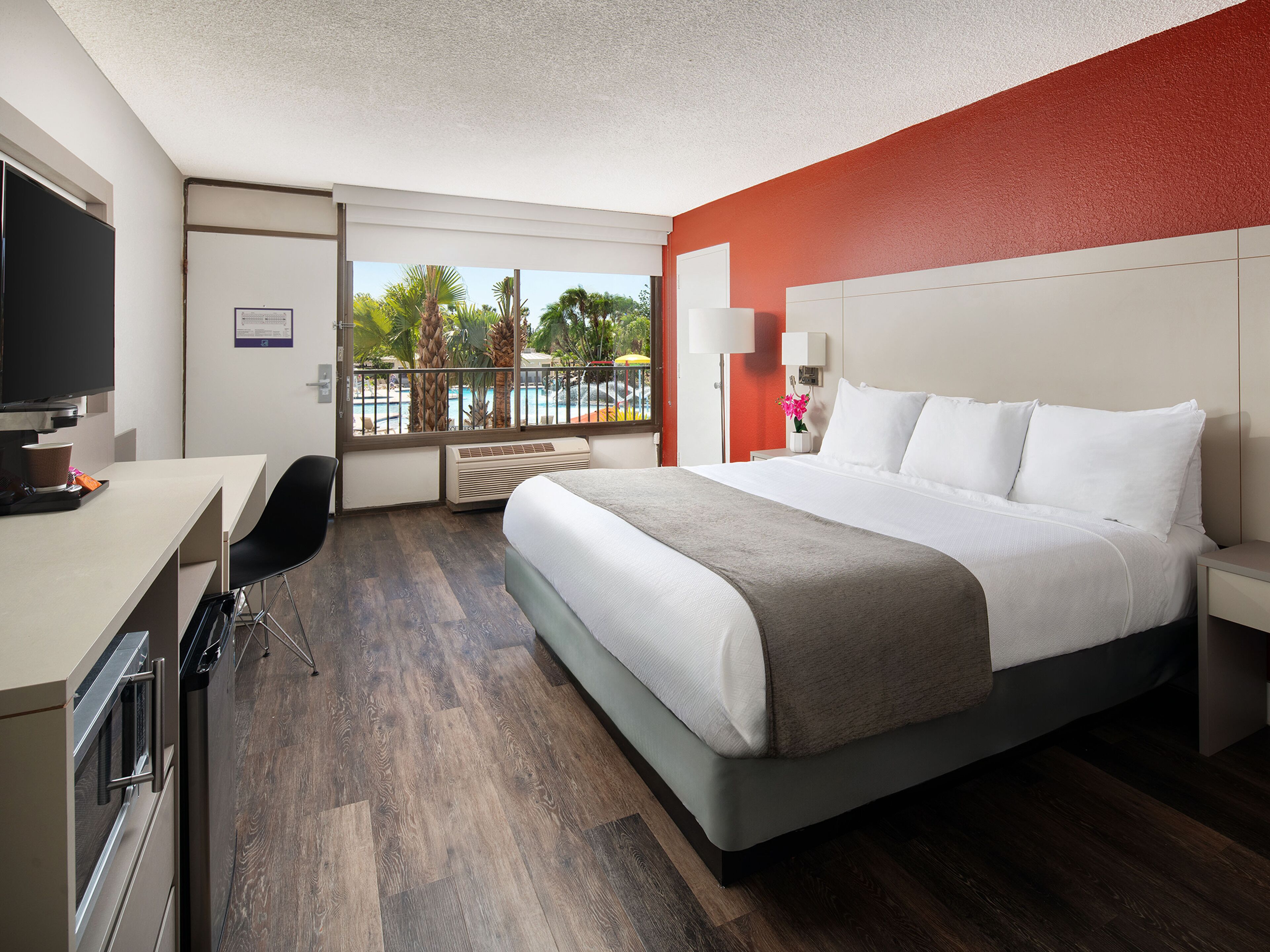 Une chambre d’hôtel avec un lit, un bureau, une chaise et une vue sur une piscine.