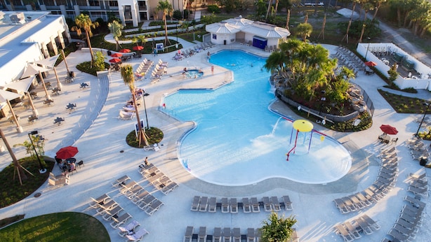 An aerial view of a resort with a large swimming pool, sun loungers, and palm trees. - Wyndham I-Drive Avanti Resort & Conference Center (Orlando)