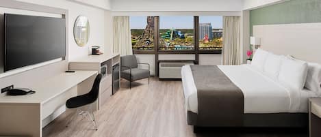 Ein Hotelzimmer mit Bett, Schreibtisch, Stuhl, Fernseher und Blick auf eine Stadtlandschaft.