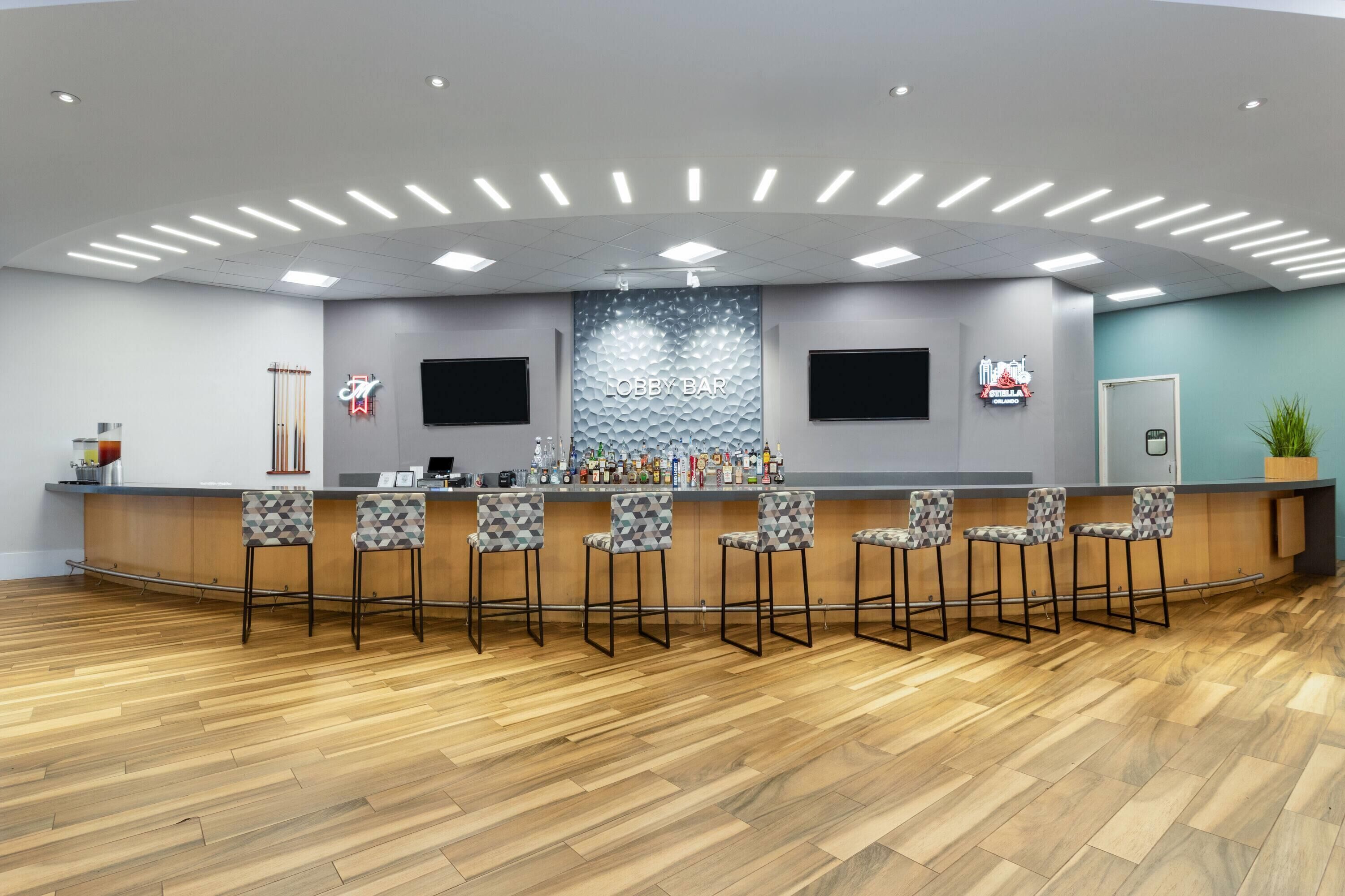 A lobby bar area with a curved counter, multiple bar stools, a wall-mounted TV, and a 'Lobby Bar' sign.